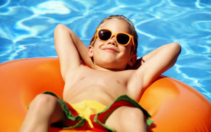 Boy wearing sun glasses, floating on a raft in a swimming pool. Photo by Alpha Media USA Portland OR