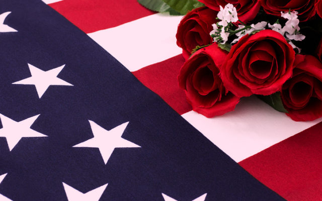 Close shot of roses laying on top and wrapped in American flag. Photo from Alpha Media USA Portland OR