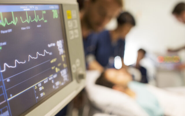 Heart rate monitor, patient and doctors in background in intensive care unit. Photo from Alpha Media Portland OR