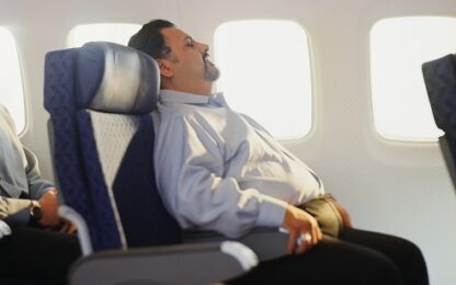 Man sleeping in an airline seat, without a face mask. Photo from Alpha Media Portland OR